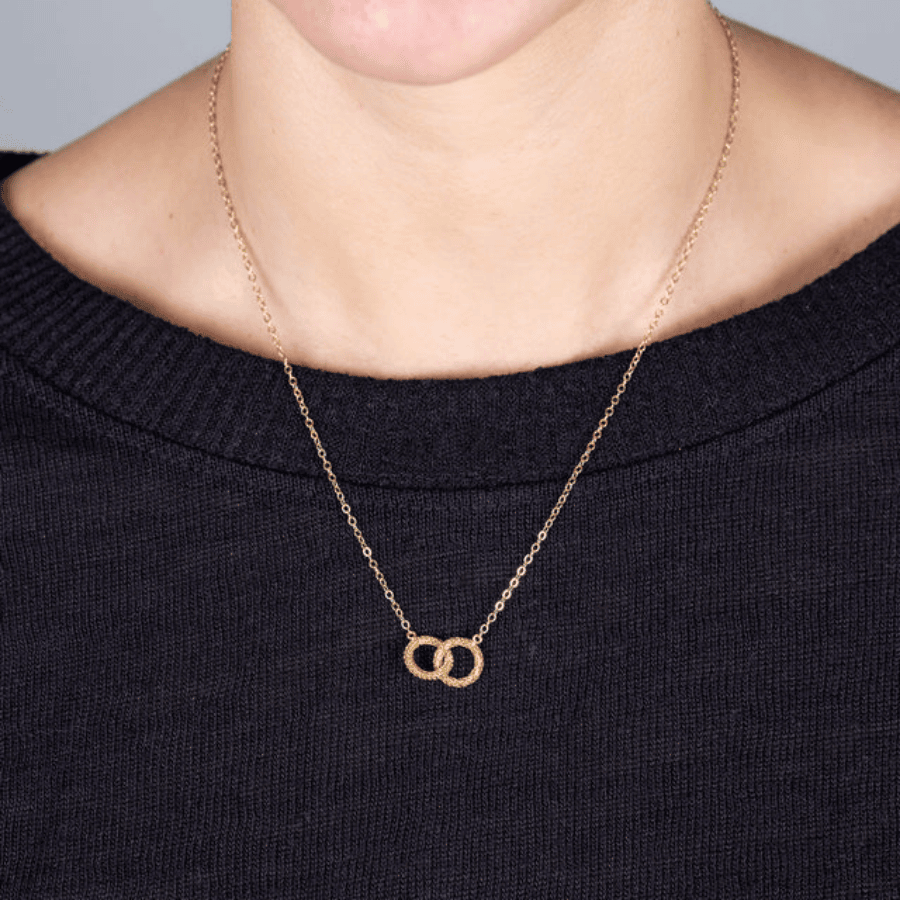 18k yellow gold necklace featuring two interlocking diamond-cut circles on a delicate chain worn against a black sweater.