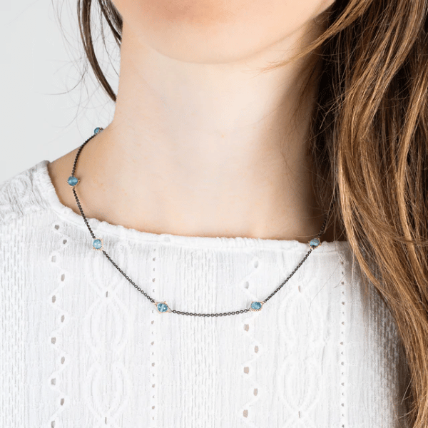 Amali station necklace featuring blue topaz stones set in 18k yellow gold on an oxidized sterling silver chain.