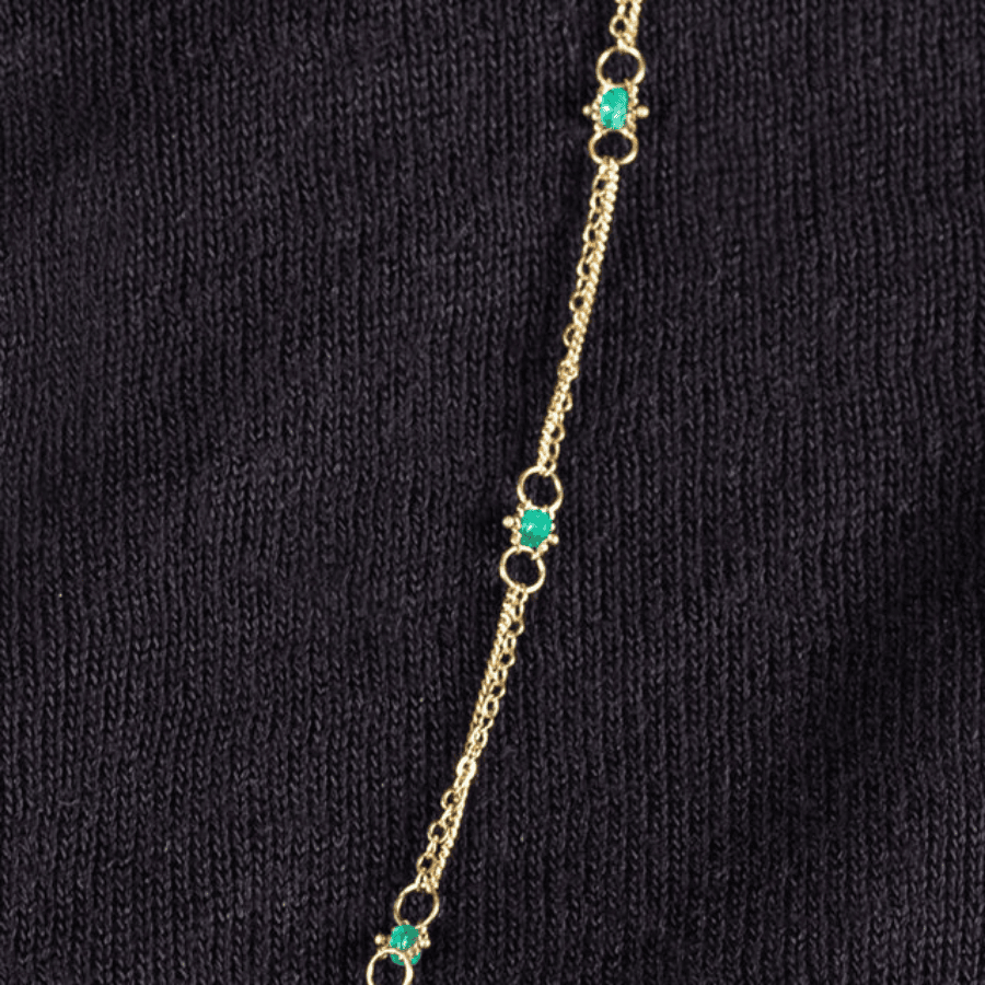 Amali 18k yellow gold chain necklace featuring hand-woven emerald stones against a black background.