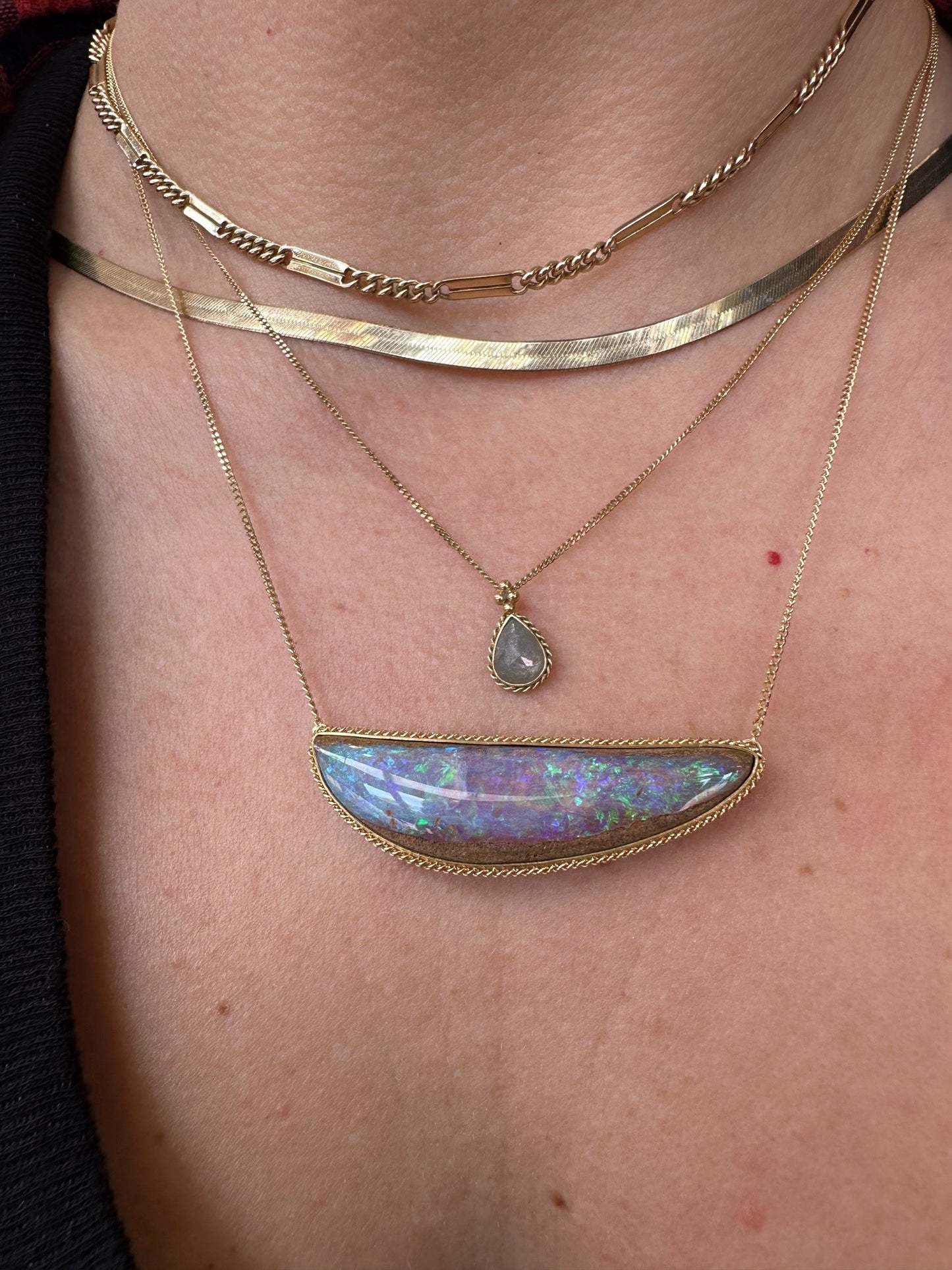Large east-west set opal pendant in 18k yellow gold on a delicate chain worn layered with other gold necklaces.