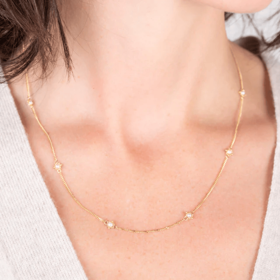 Delicate 18k yellow gold station necklace featuring small freshwater pearls on a hand-woven chain worn around the neck.