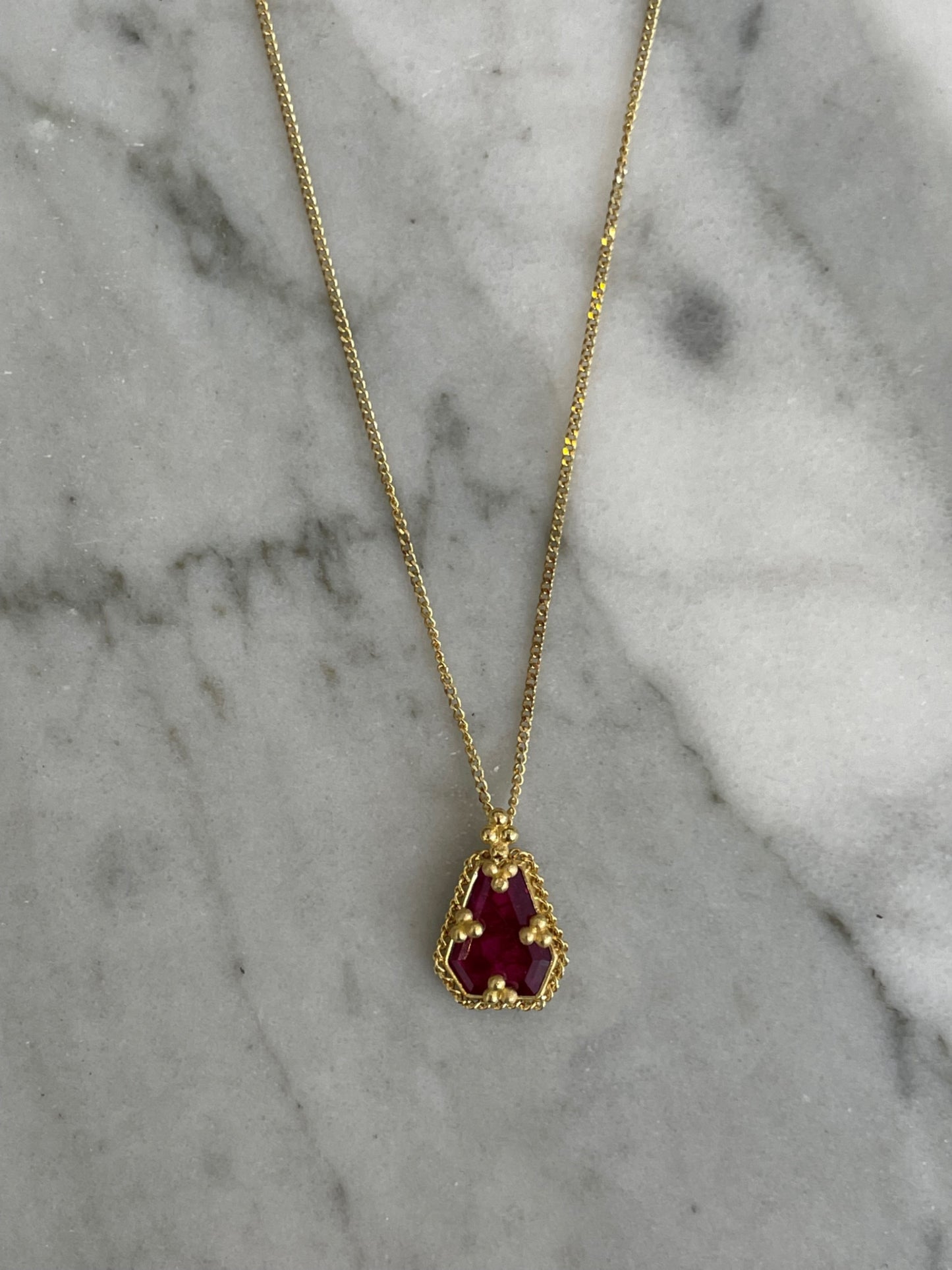 18k yellow gold necklace featuring a faceted ruby slice pendant on a delicate gold chain against a marble background.