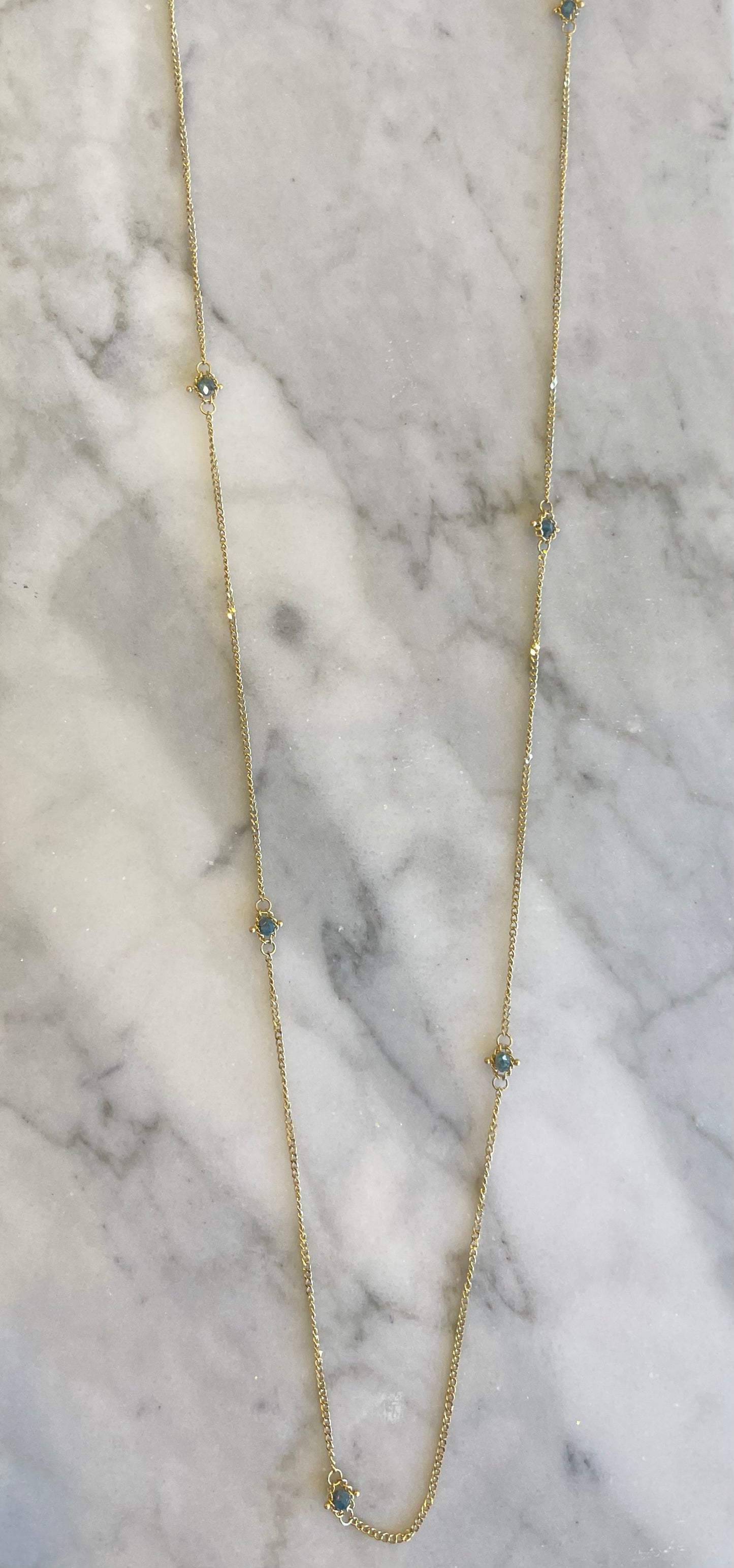 18k yellow gold station chain necklace with handwoven silver diamonds on a marble surface.