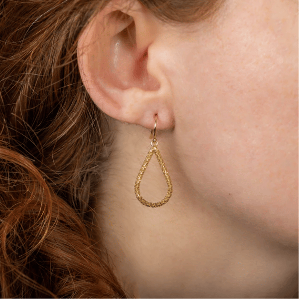 Hand-woven 18k yellow gold teardrop earrings with a textured diamond-cut finish on a French hook, worn on an earlobe.