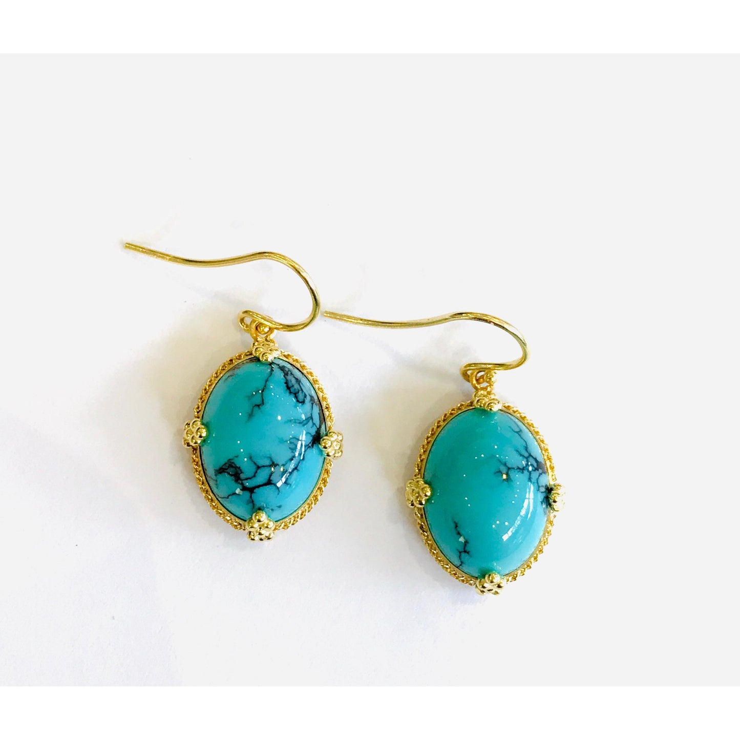 Oval turquoise earrings with black veining set in ornate 18k yellow gold frames on gold hooks.