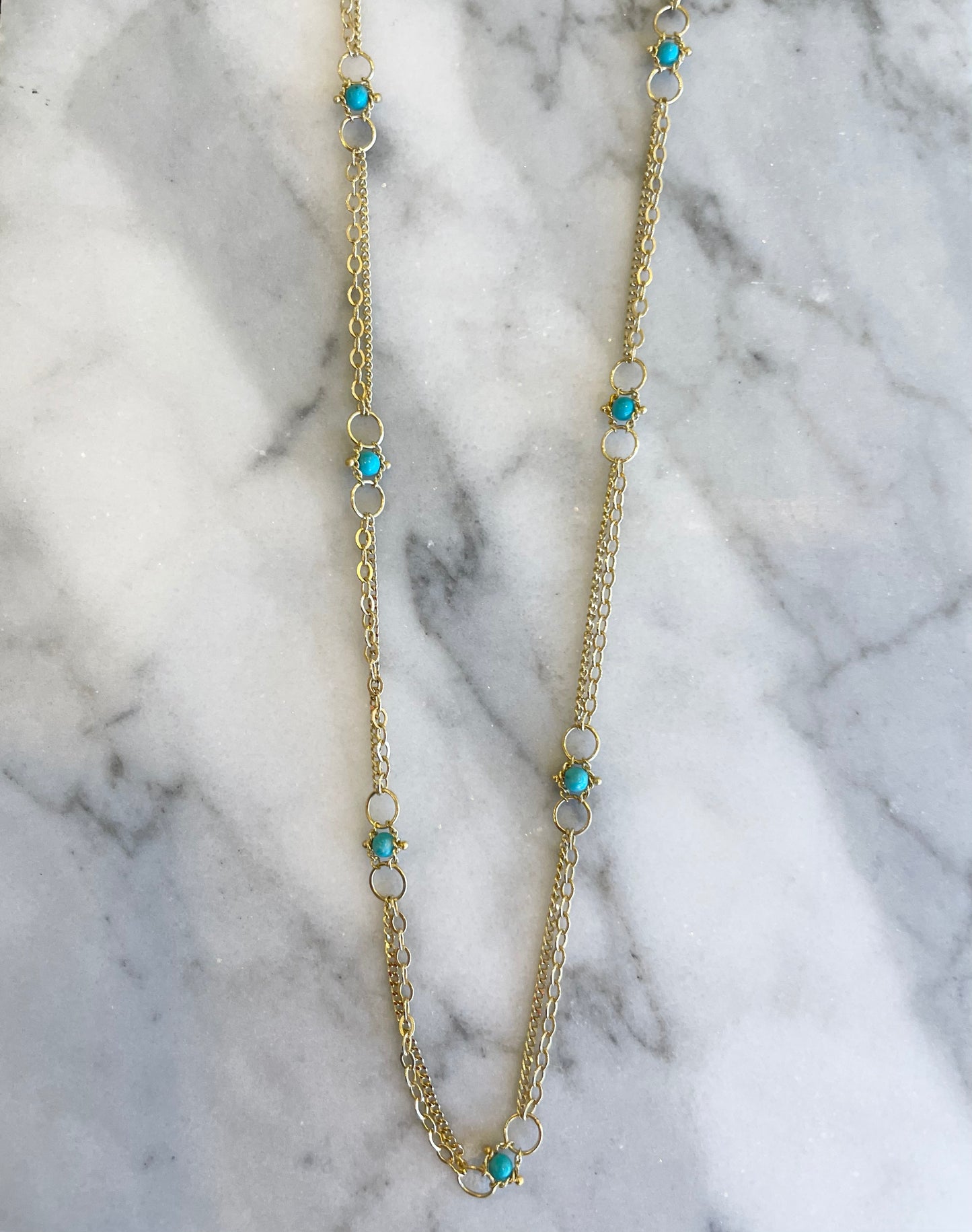 18k yellow gold chain necklace featuring delicate turquoise stones set between small gold hoops on a marble surface.