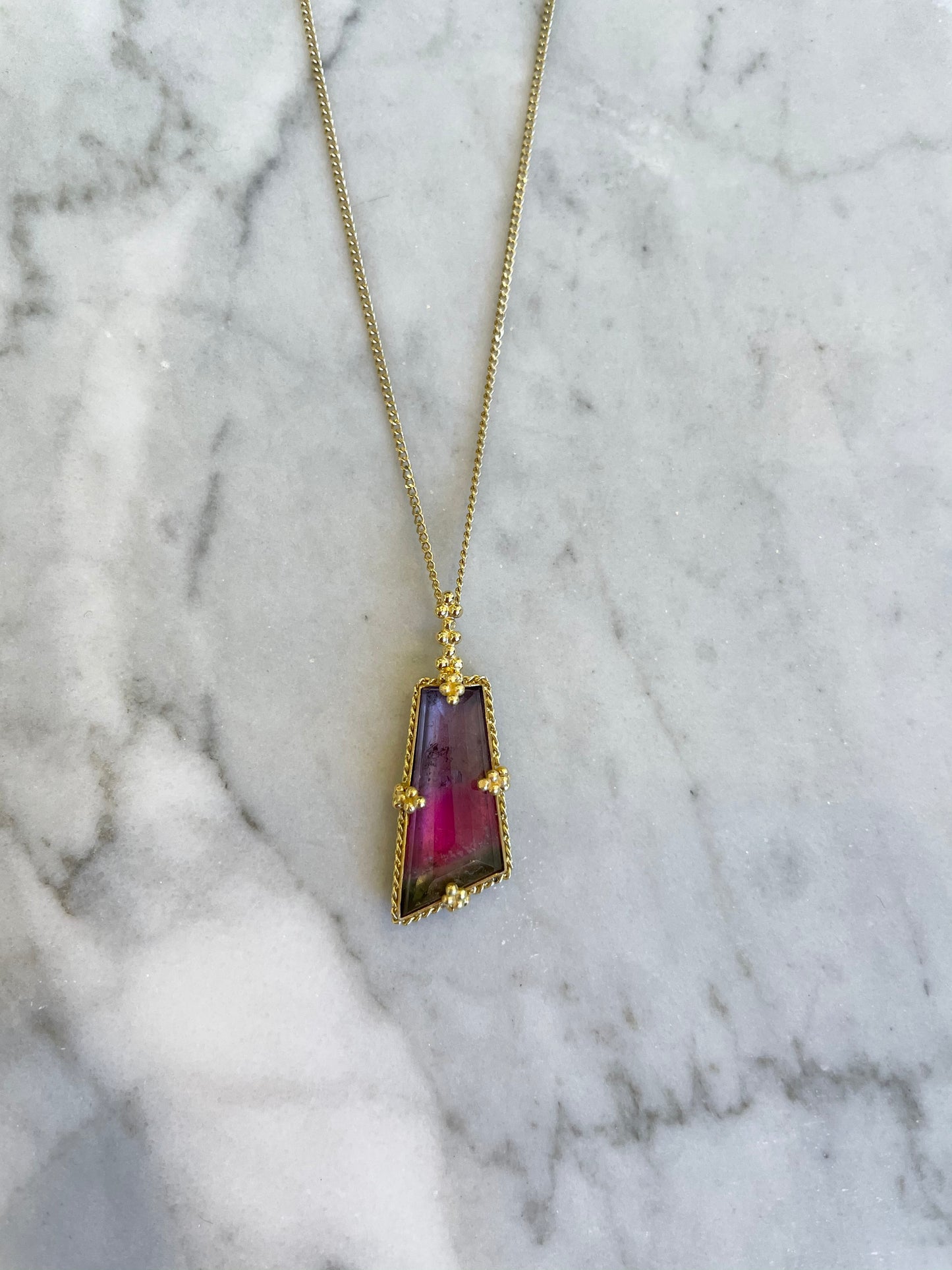 5.96ct watermelon tourmaline pendant in 18k yellow gold on a delicate gold chain against a white marble background.