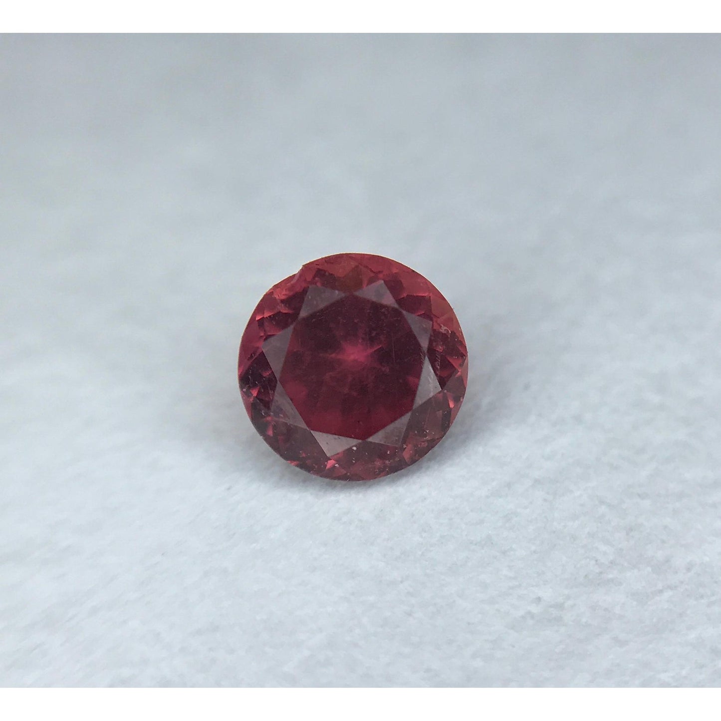 0.59 carat round pink sapphire gemstone with brilliant facets on a white background.