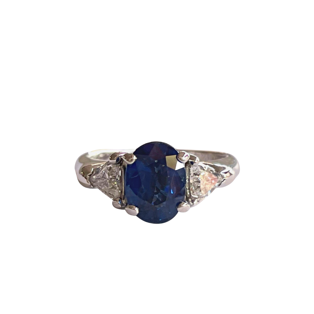 14k white gold ring featuring a 1.41ct oval sapphire center stone flanked by two trillion-cut diamonds.