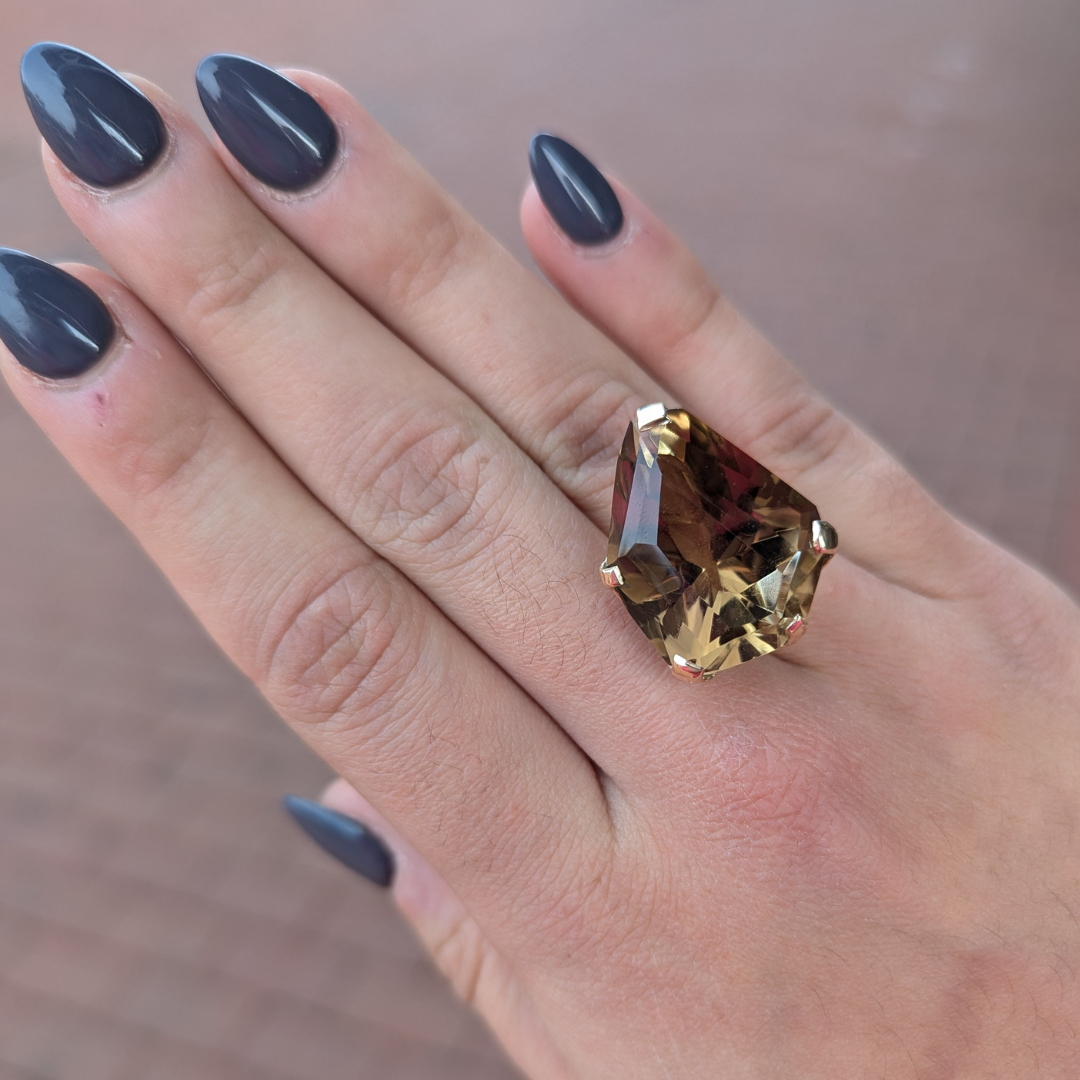 Large 35ct freeform smoky quartz ring set in 14k yellow gold, worn on a finger with dark grey nail polish.