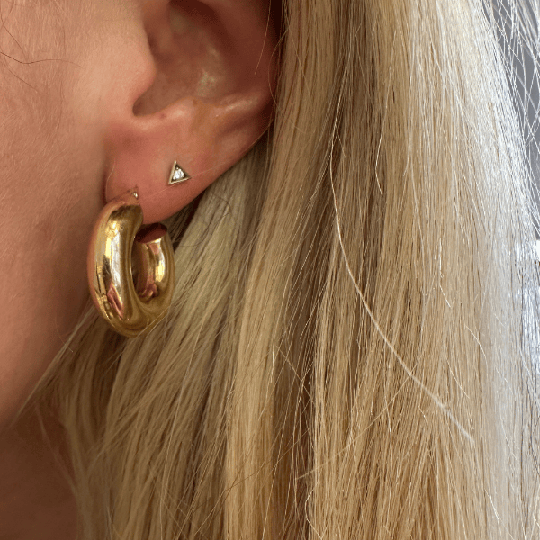 6.5mm wide chunky 14k yellow gold hoop earrings worn on an earlobe.