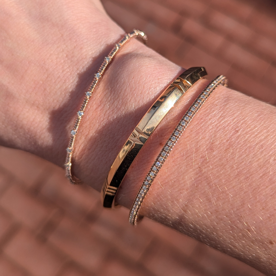 Tiffany & Co. 18k rose gold Atlas bangle with Roman numeral engravings, worn on a wrist with two diamond-accented bracelets.