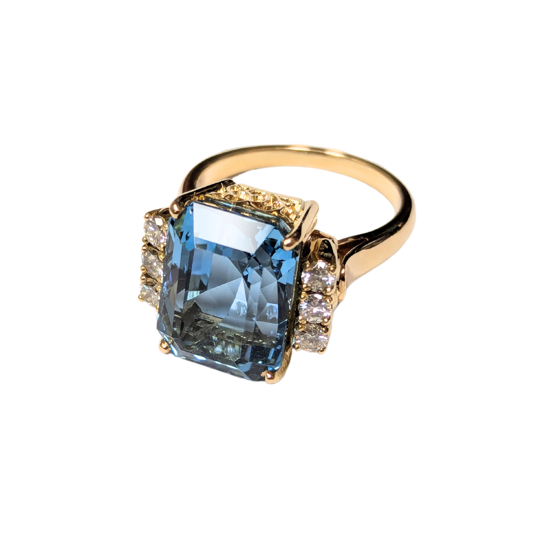 18k yellow gold ring featuring a large emerald-cut aquamarine flanked by six round brilliant-cut diamonds.