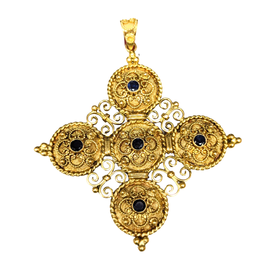 18k yellow gold baroque filigree cross pendant featuring five round blue sapphires in an intricate textured design.