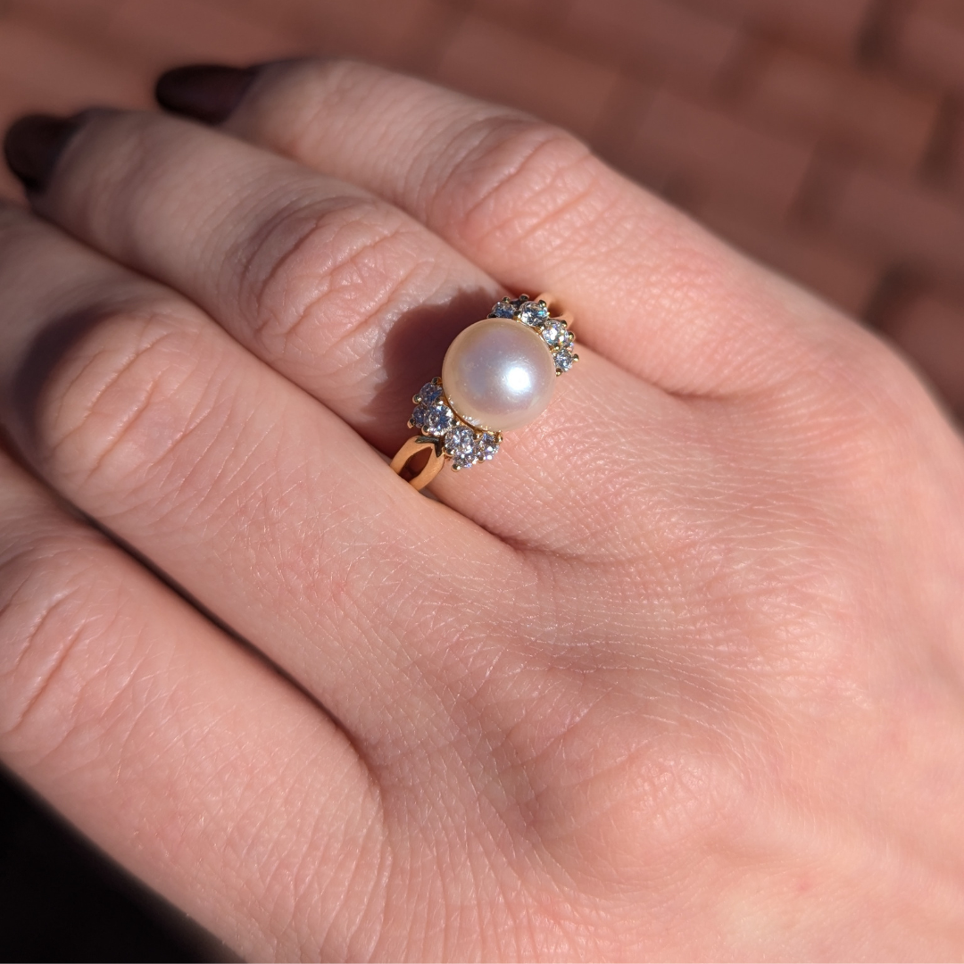 18k yellow gold ring featuring a central cultured pearl flanked by sparkling round brilliant diamond accents.