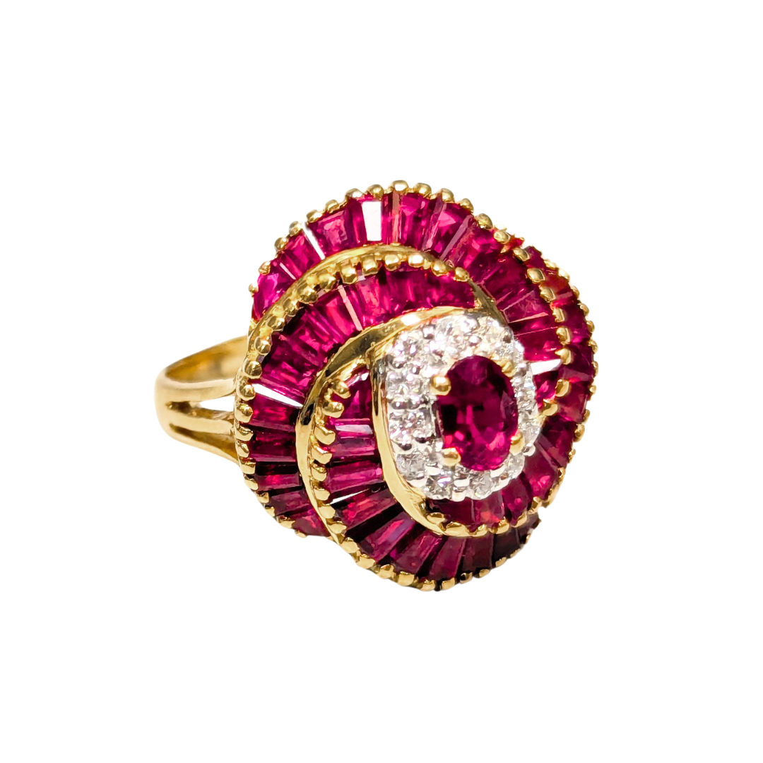 18k yellow gold ballerina ring featuring an oval ruby, diamond halo, and tiered baguette ruby surround.