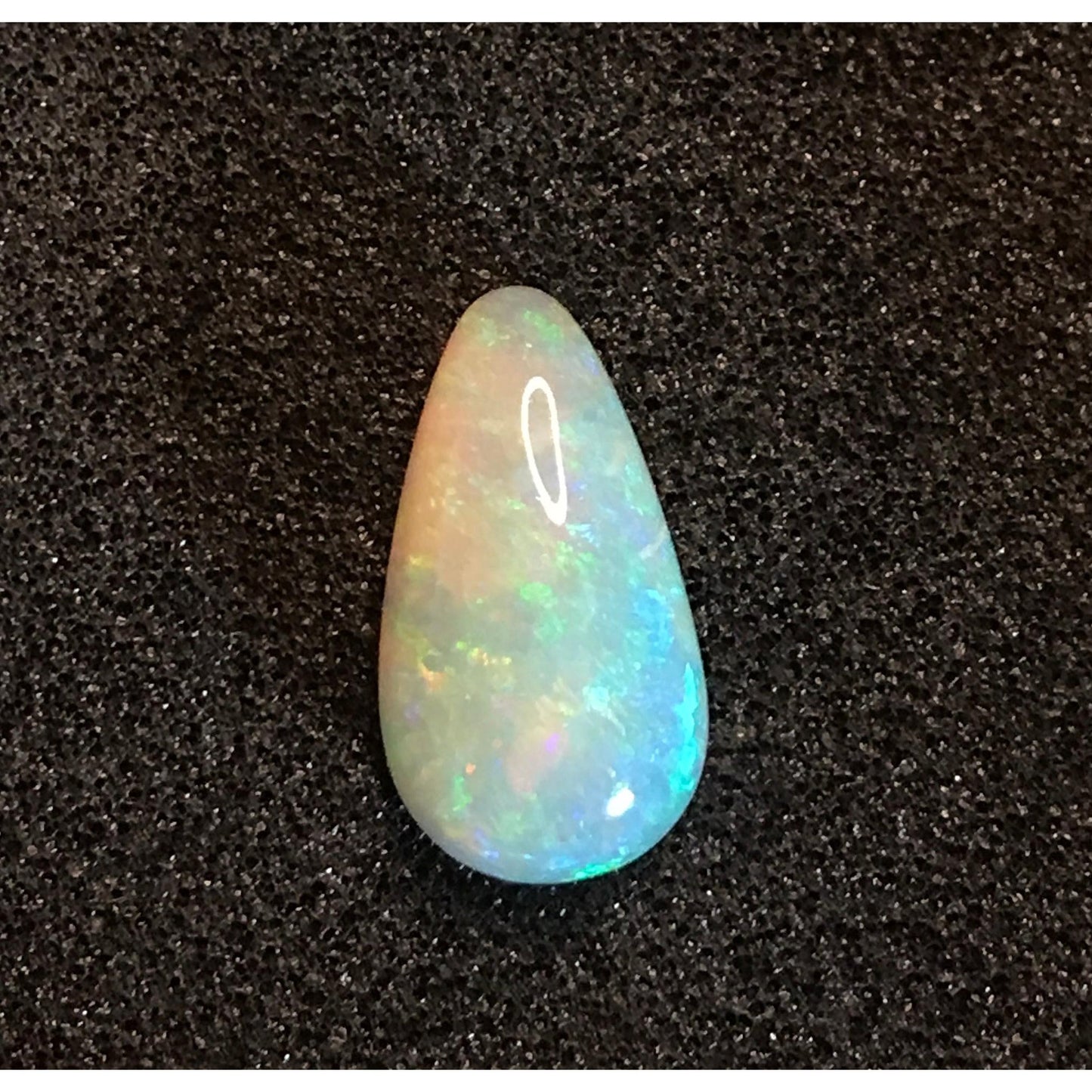 2.40 carat pear-shaped opal gemstone with iridescent blue and green flashes on a black textured background.