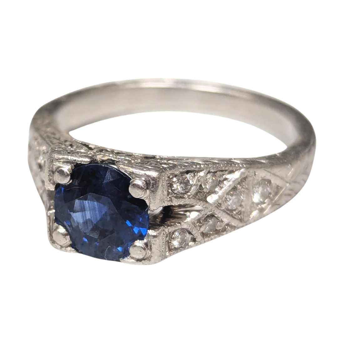 Art Deco platinum ring featuring a round blue sapphire center stone and engraved diamond-set shoulders.