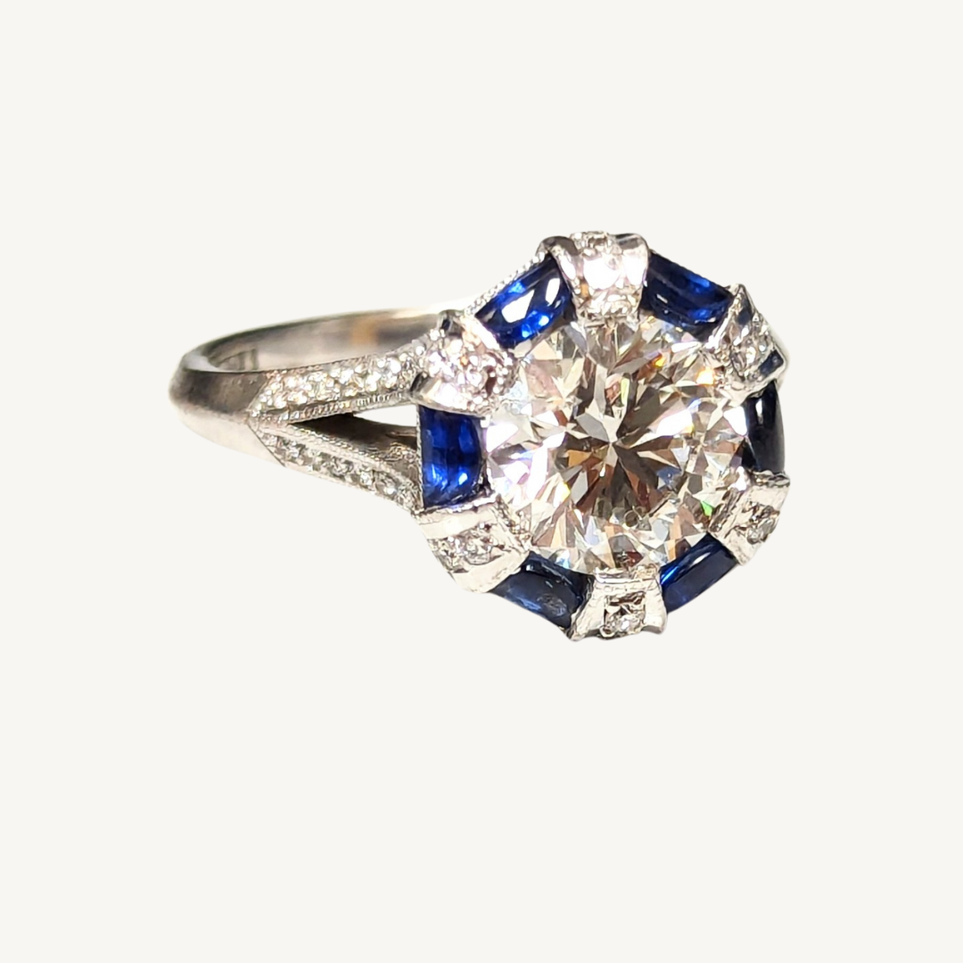 Art Deco 18k white gold ring featuring a 1.88ct diamond center, blue sapphire cabochons, and diamond accents.