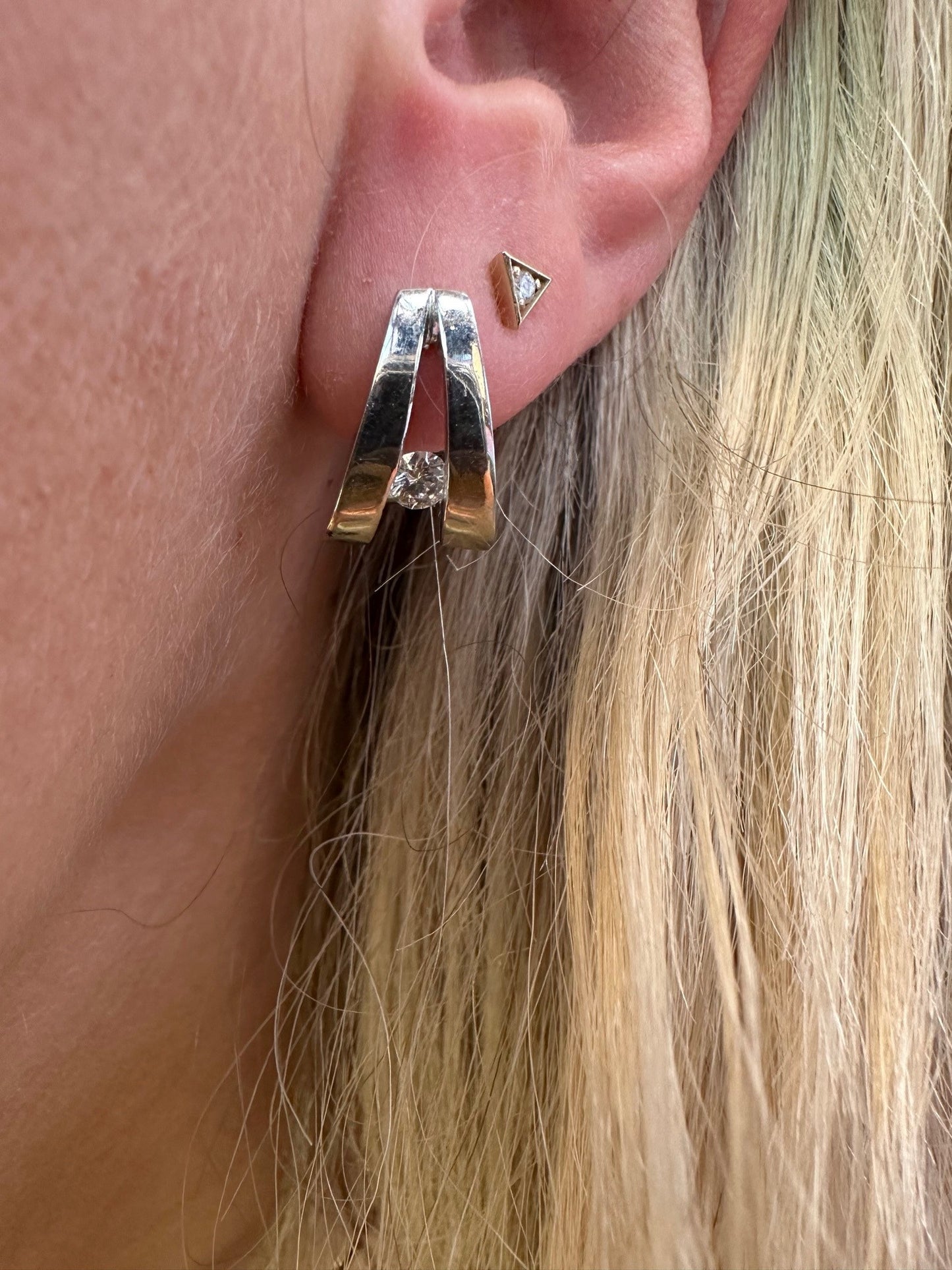 John Atencio platinum hoop earrings featuring a round brilliant cut diamond worn on a blonde woman's ear.