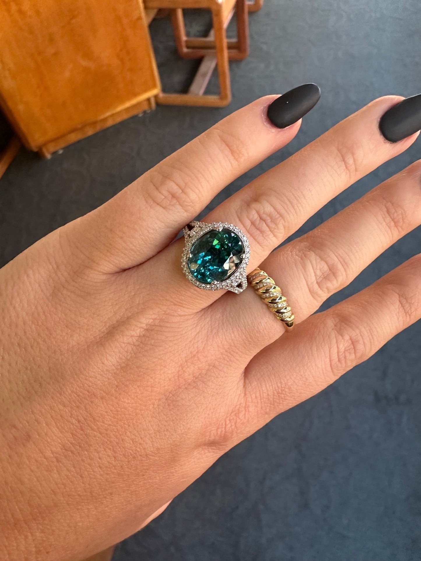 18k white gold ring featuring a 4.68ct oval greenish-blue tourmaline surrounded by 0.77ct round brilliant diamonds.