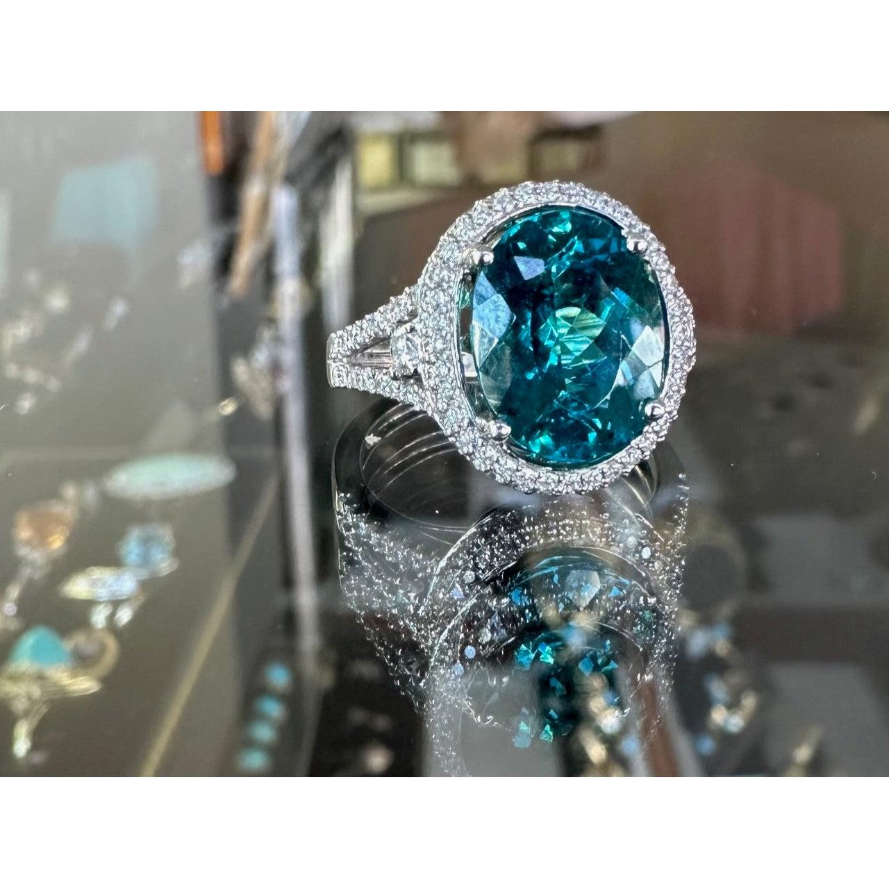 Oval greenish-blue tourmaline ring in 18k white gold with a diamond halo and pavé band.
