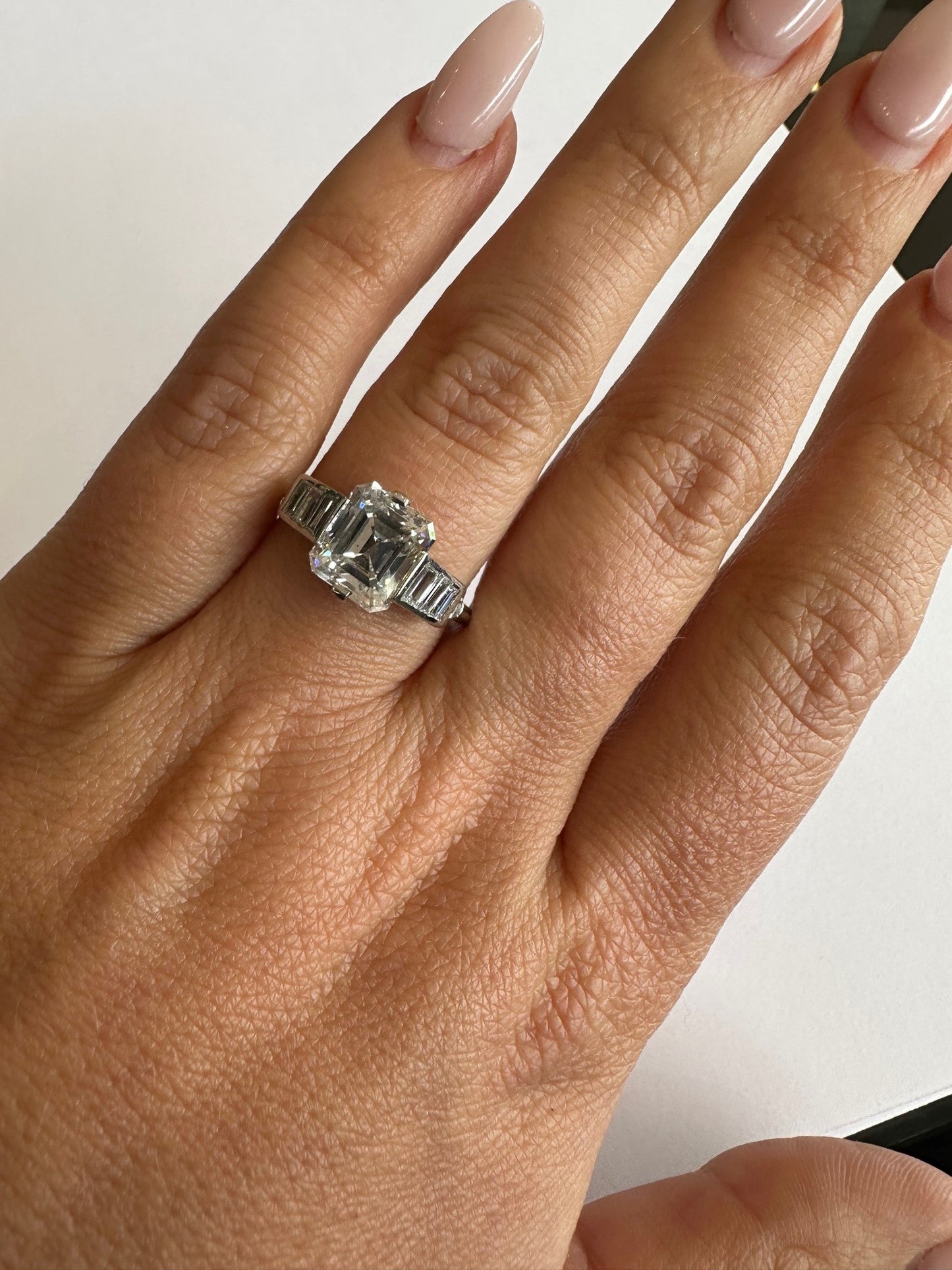 Platinum ring featuring a 2.62ct emerald cut diamond center flanked by baguette diamonds on a finger.