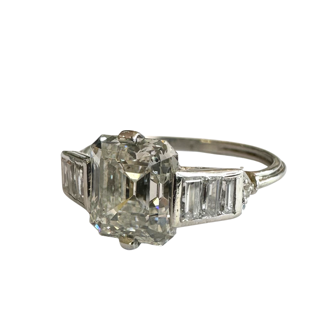 Platinum ring featuring a 2.62ct emerald cut diamond center flanked by baguette and single cut diamonds.