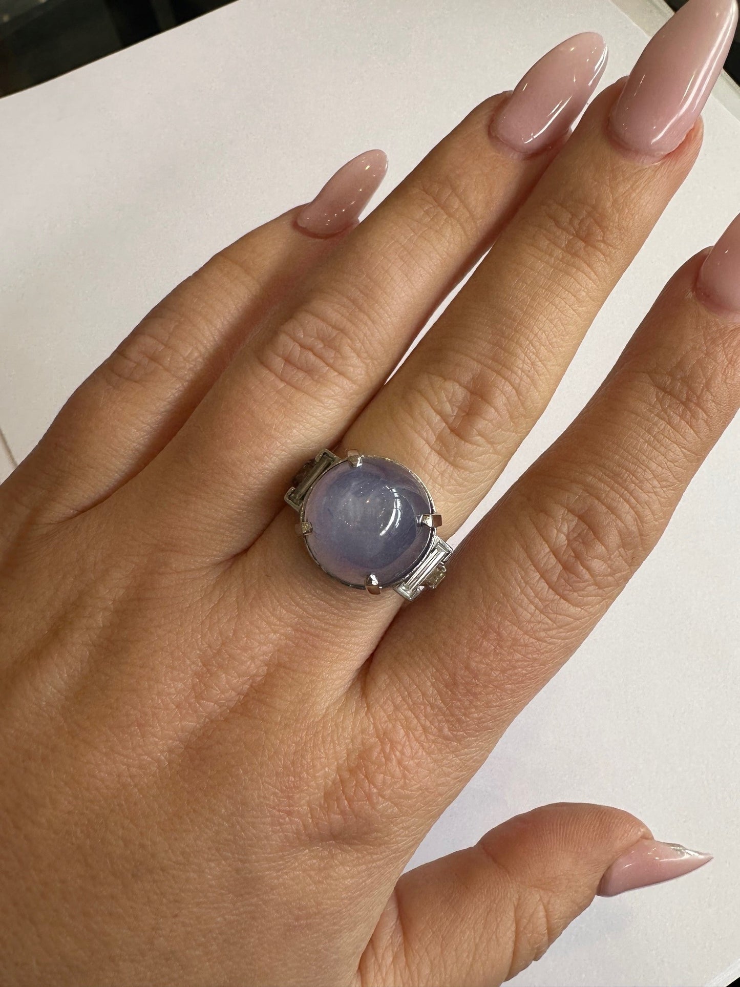 Platinum ring featuring a large round purple star sapphire accented by four baguette-cut diamonds on a finger.
