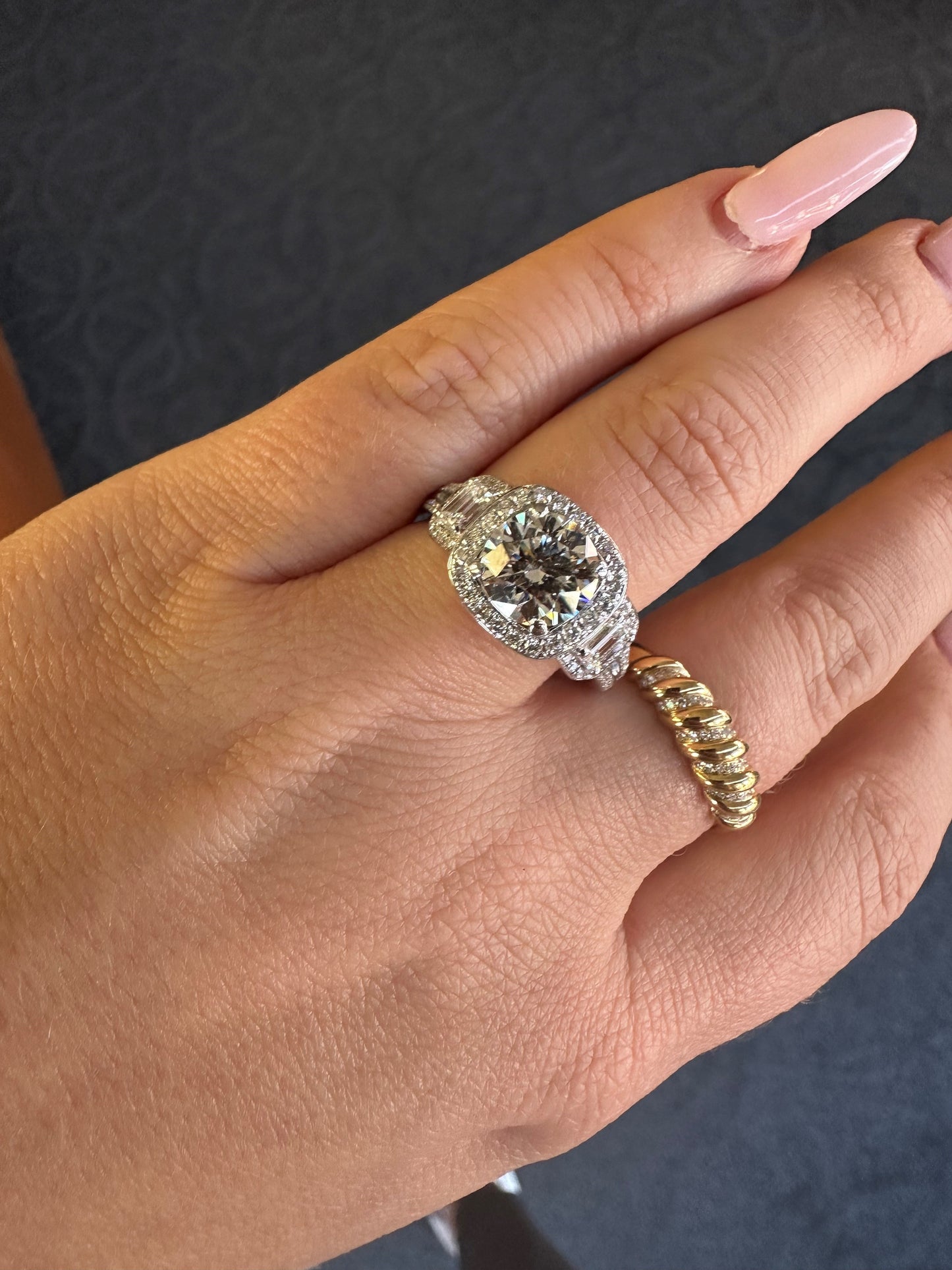 18k white gold three-stone diamond halo ring with round and emerald cut diamonds worn on a finger.