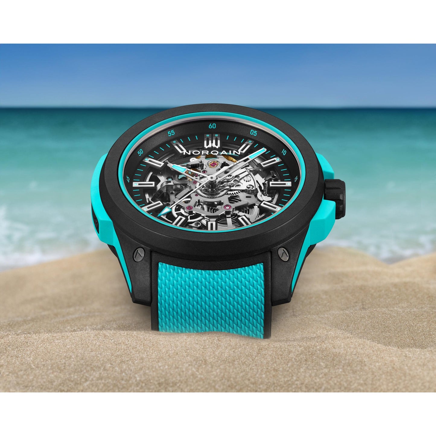NORQAIN Wild ONE Skeleton 42mm watch with black NORTEQ carbon fiber case and turquoise rubber accents on a sandy beach.